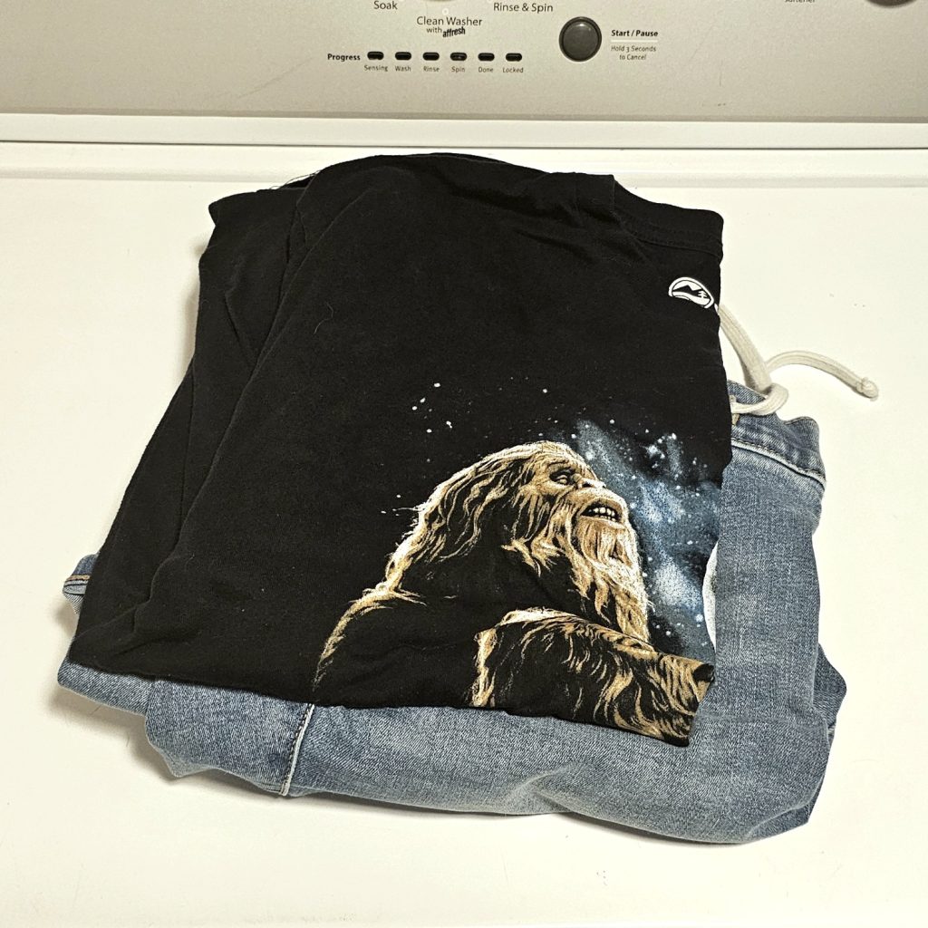 A T-shirt with Bigfoot on it stacked on top of a pair of jeans.